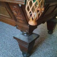 Corner shot displaying both the drop pockets and the distinctly beautiful hand carved body of this antique Brunswick pool table.