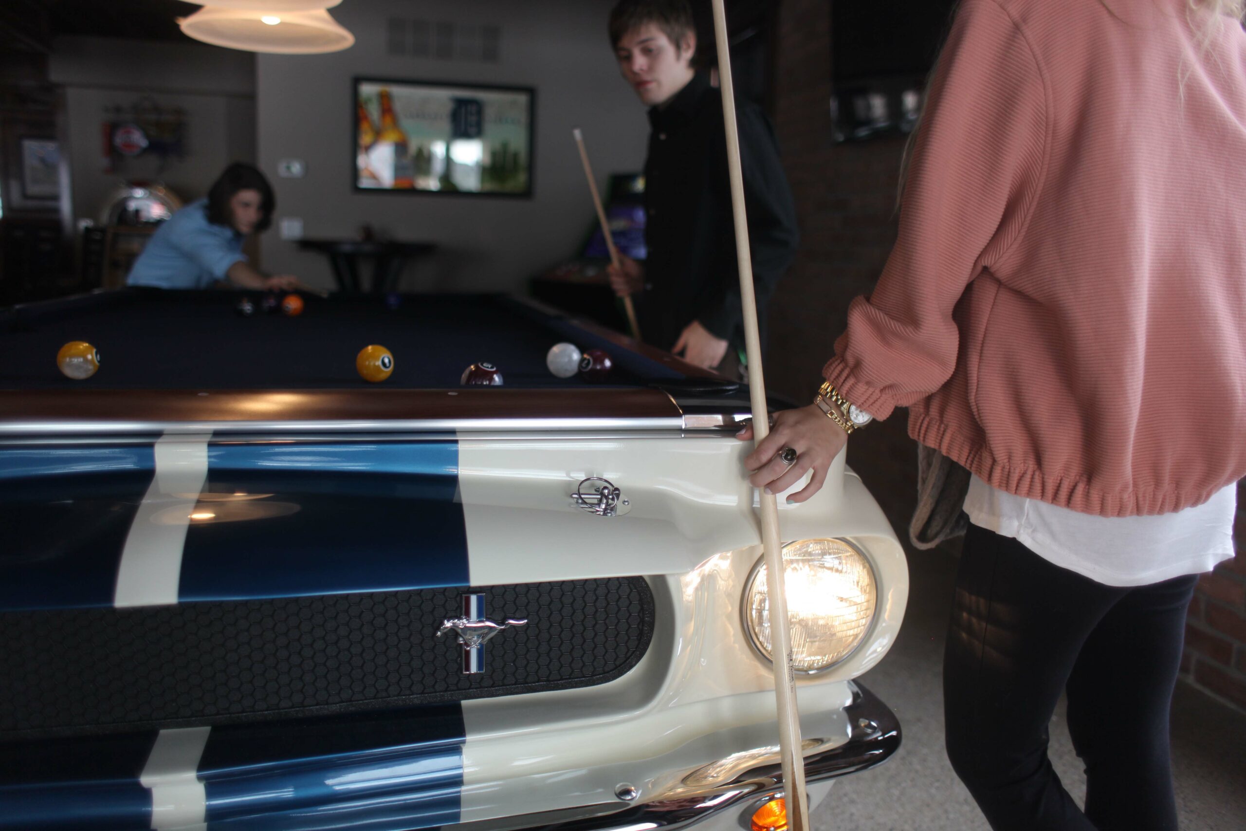 working headlights shown on the front right of a Ford Shelby GT-350 car pool table. Teens playing pool.