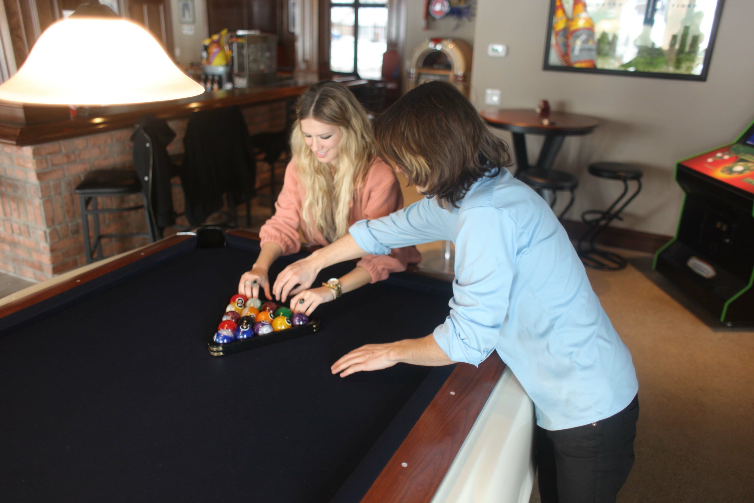Two women racking a set of billiard balls getting ready for a game of 8 ball.