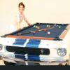 Woman leaning on a beautiful 1965 Shelby GT-350 car pool table with wood grain top rails in white with blue racing stripes.