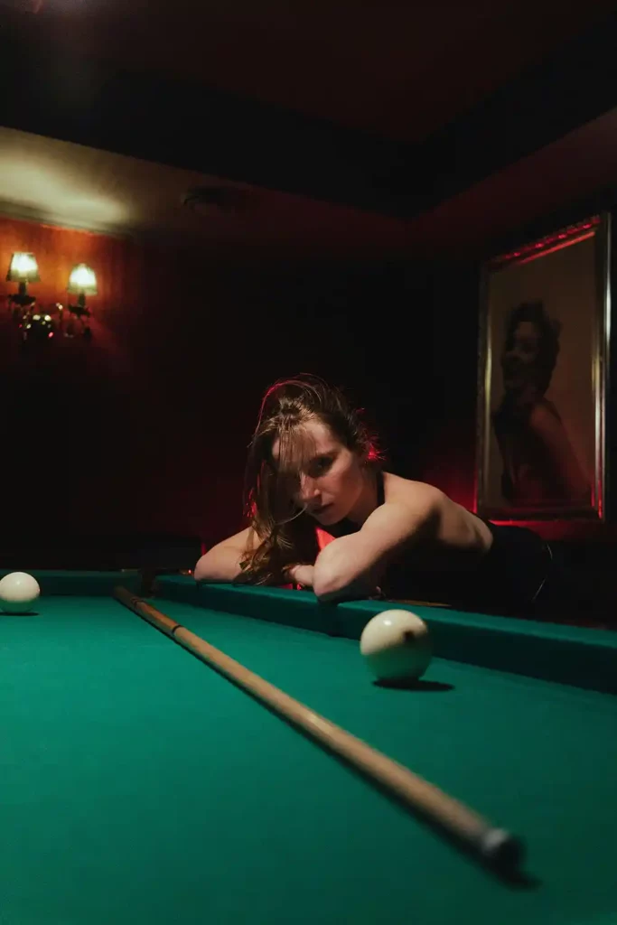 pool player sitting next to pool table looking at her cue on the table and contemplating the specifications that make up her high end used pool cue.